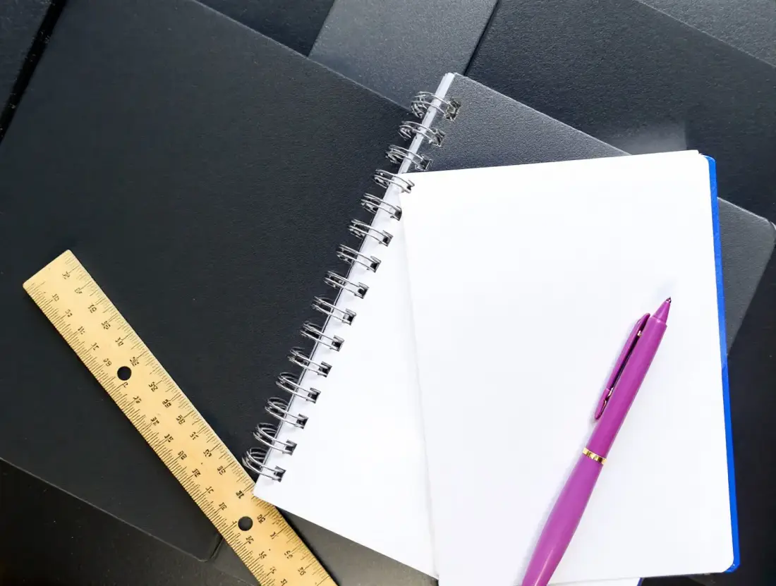 Otwarty notes z linijką i różowym długopisem na grafitowym biurku