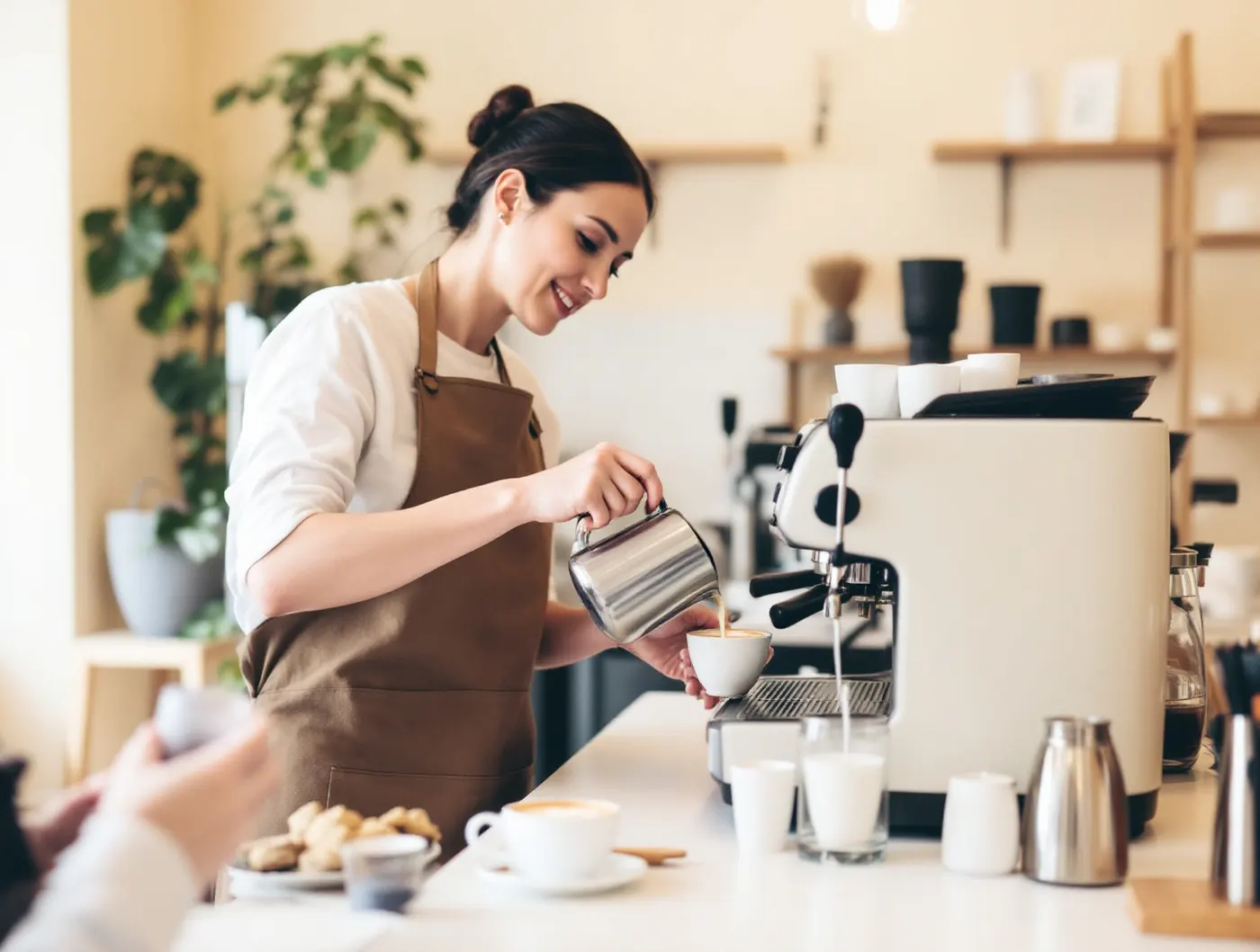 Instruktorka w brązowym fartuchu nalewa latte art podczas warsztatów
